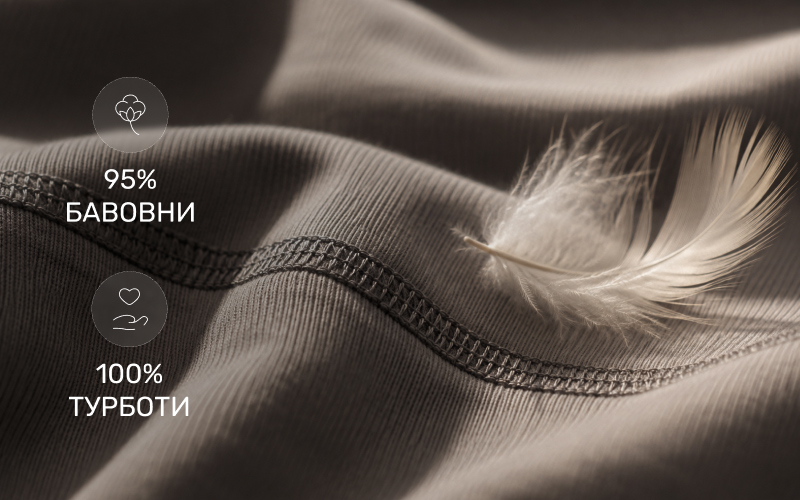 Макрозйомка м'якої сірої трикотажної тканини в рубчик з акуратним швом, на якій лежить невагома біла пір'їнка, що підкреслює натуральний склад білизни (95% бавовни) та її легкість.