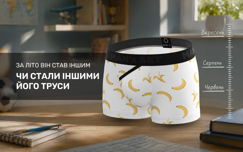 Дитячі білі боксери з яскравим принтом бананів та чорною резинкою, розміщені на фоні дитячої кімнати з підручниками. Праворуч зображена графічна шкала зросту дитини за літні місяці: червень, серпень та вересень.