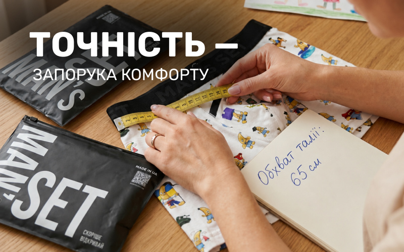 Процес вимірювання жовтою сантиметровою стрічкою резинки дитячих трусів з принтом бананів. Поруч лежить блокнот із записом про обхват талії 65 см та фірмові чорні зіп-пакети Man's Set.