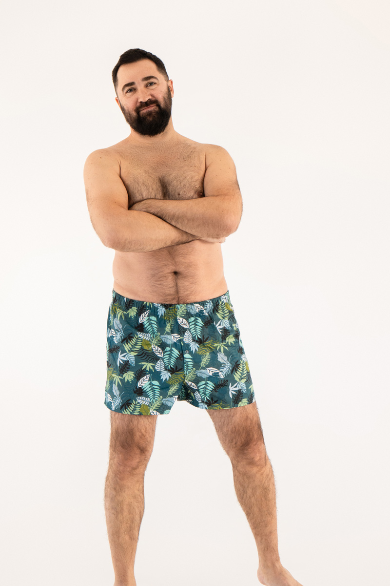 Улыбающийся бородатый мужчина в свободных мужских трусах (семейках) с тропическим принтом листьев.