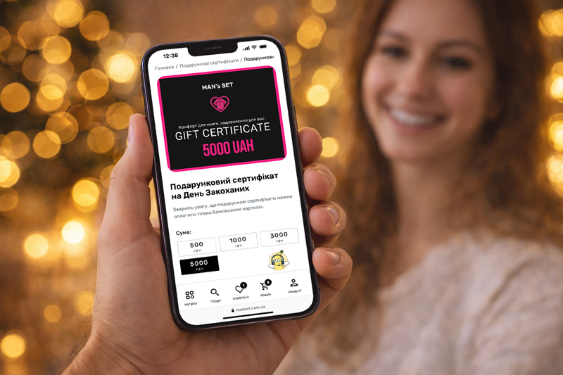 Электронный сертификат изображен на экране смартфона, на фоне изображена девушка, которая подарила сертификат любимому мужчине.