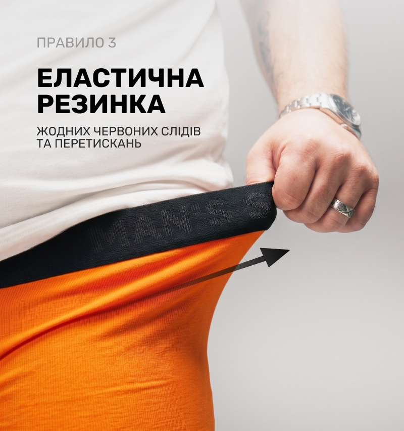 Чоловік відтягує широку еластичну чорну резинку помаранчевих трусів, демонструючи еластичність виробу та відсутність передавлювання шкіри.